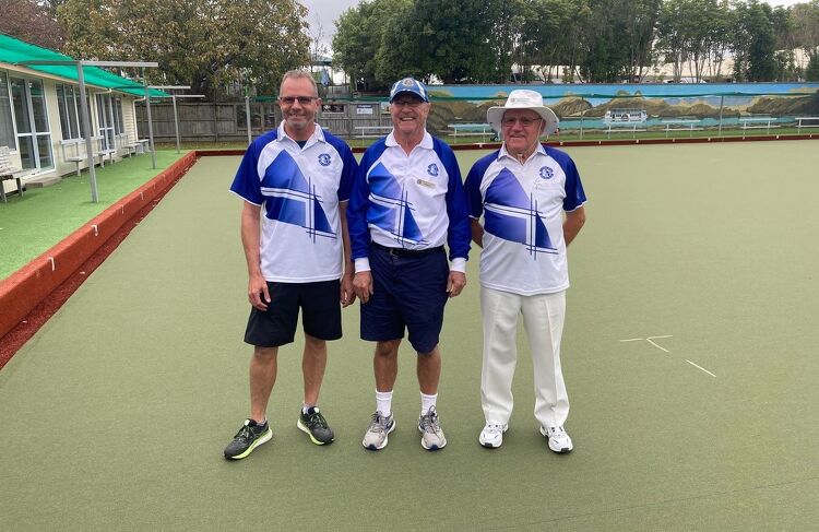 Three male members of the Claudelands Bowling Club, dressed in matching blue and white uniforms, standing side-by-side on the green, smiling at the camera.